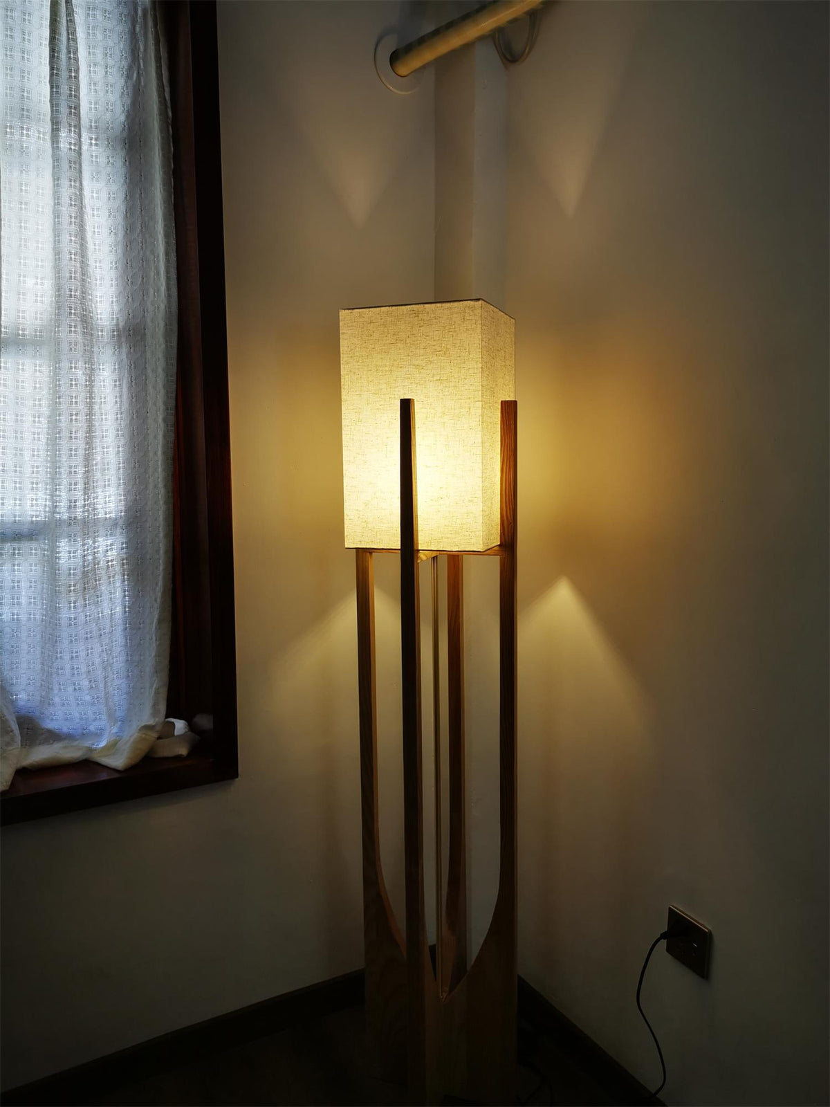 Lit Clérachic floor lamp in a dim corner by a window with sheer curtains, its glow warming the walls.