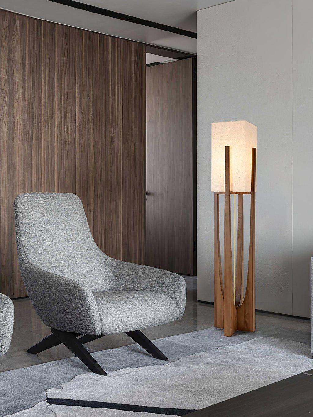 Floor lamp from Clérachic with a pale fabric shade, standing beside a grey lounge chair on a grey rug in front of wood panelling.
