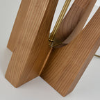 Close view of the cross-shaped wooden base of this Clérachic lamp, with the brass rod rising from its centre.