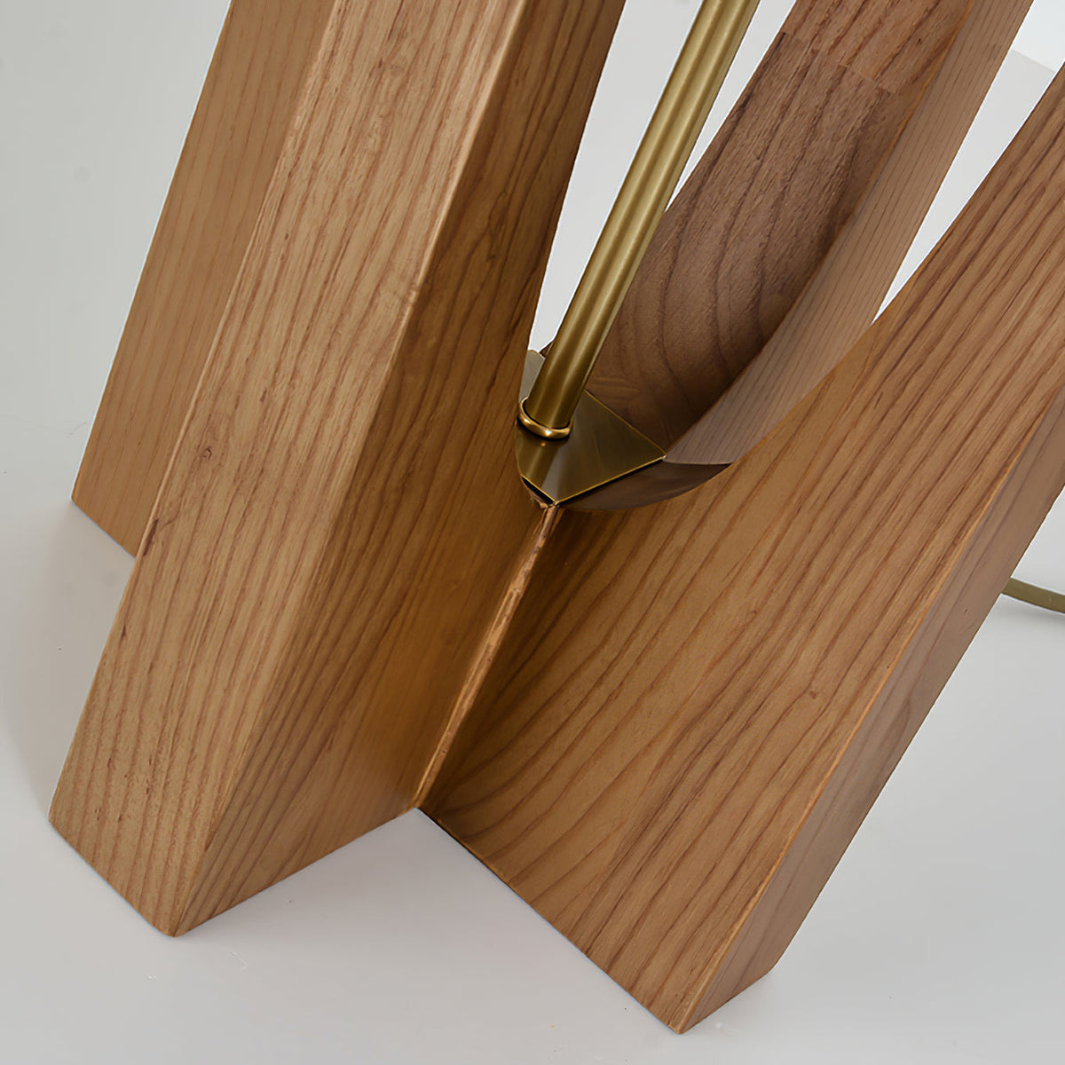 Close view of the cross-shaped wooden base of this Clérachic lamp, with the brass rod rising from its centre.