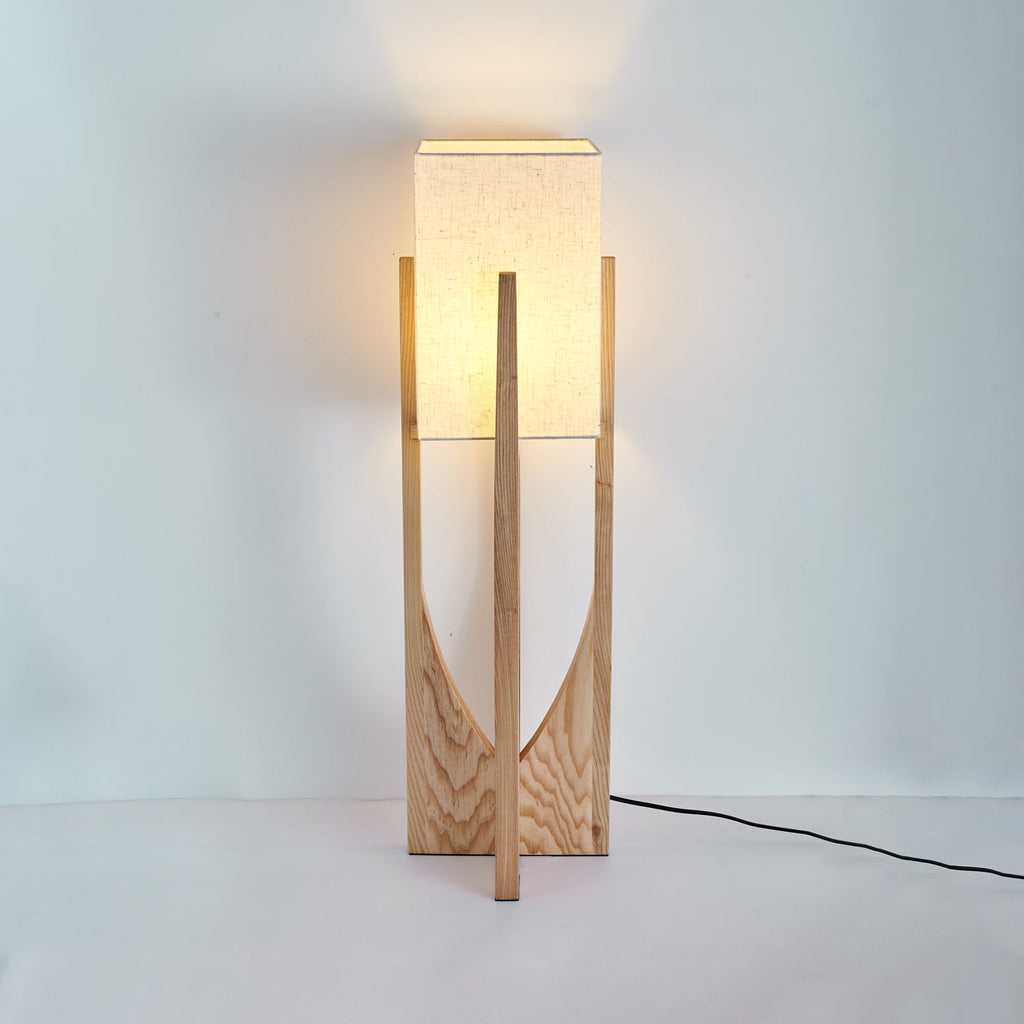 Short Clérachic table lamp in a slightly darker wood, glowing warmly, with its black cord running out to the right.