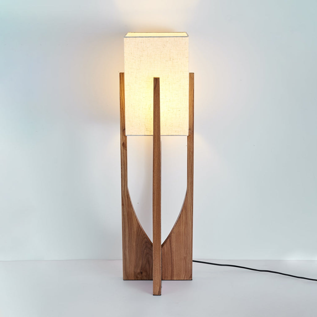 Short dark wood Clérachic lamp, lit, with a warm glow on the wall above and a black cord on the floor.