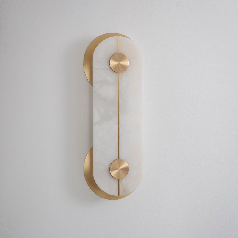 Clérachic Auriel wall light seen straight on, its alabaster capsule cradled by two brushed brass crescents on a pale grey wall.