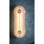 The Clérachic sconce lit against a deep teal plaster backdrop, warm light pooling through the alabaster and around the brass discs.
