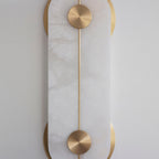 Clérachic Auriel in tight detail, the brushed brass disc and slender rod set flush against the cool white alabaster face.