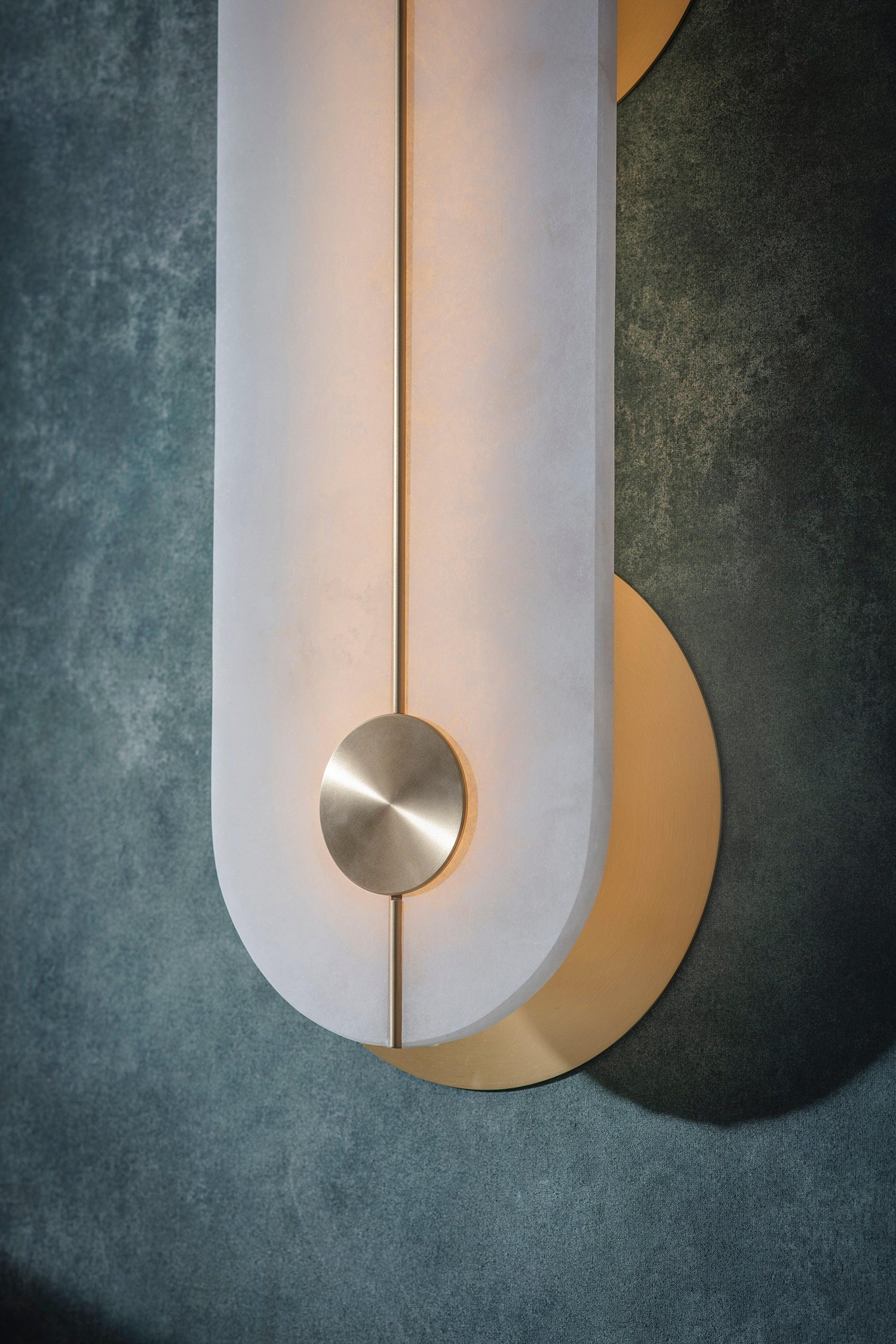 The Clérachic sconce in macro, showing how the brass crescent sits behind the lit alabaster and the rod meets the brushed disc.