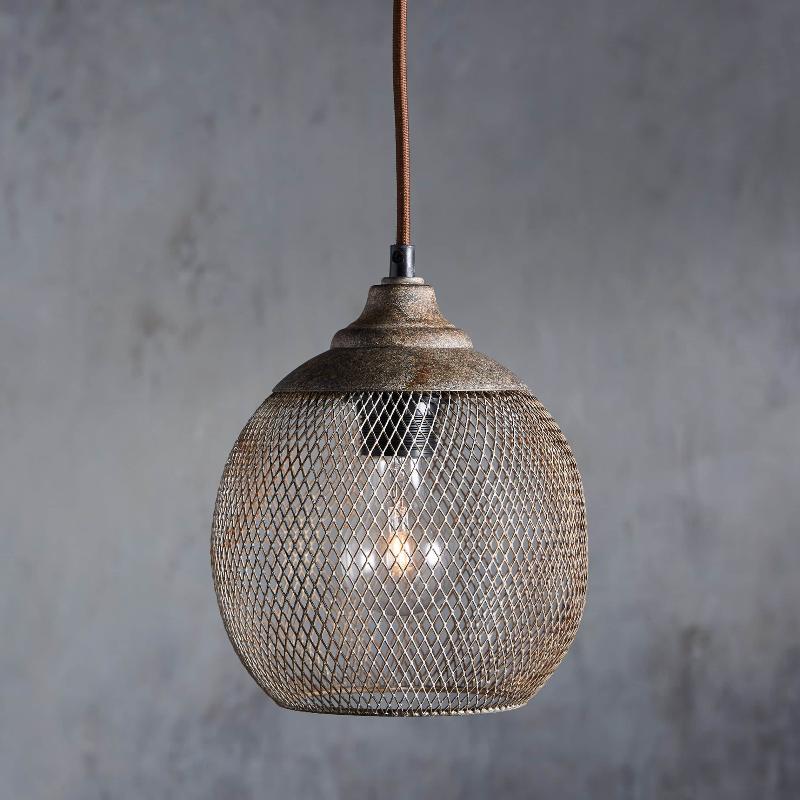 A Clérachic rust mesh pendant glows softly against a weathered gray backdrop.