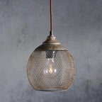 A Clérachic rust mesh pendant glows softly against a weathered gray backdrop.
