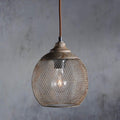A Clérachic mesh pendant in the smaller size hangs against a weathered gray wall.