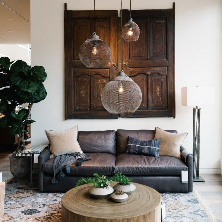 Clérachic mesh pendants cluster above a leather sofa and a carved wood door panel.