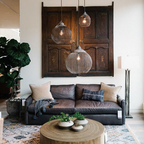Clérachic mesh pendants cluster above a leather sofa and a carved wood door panel.