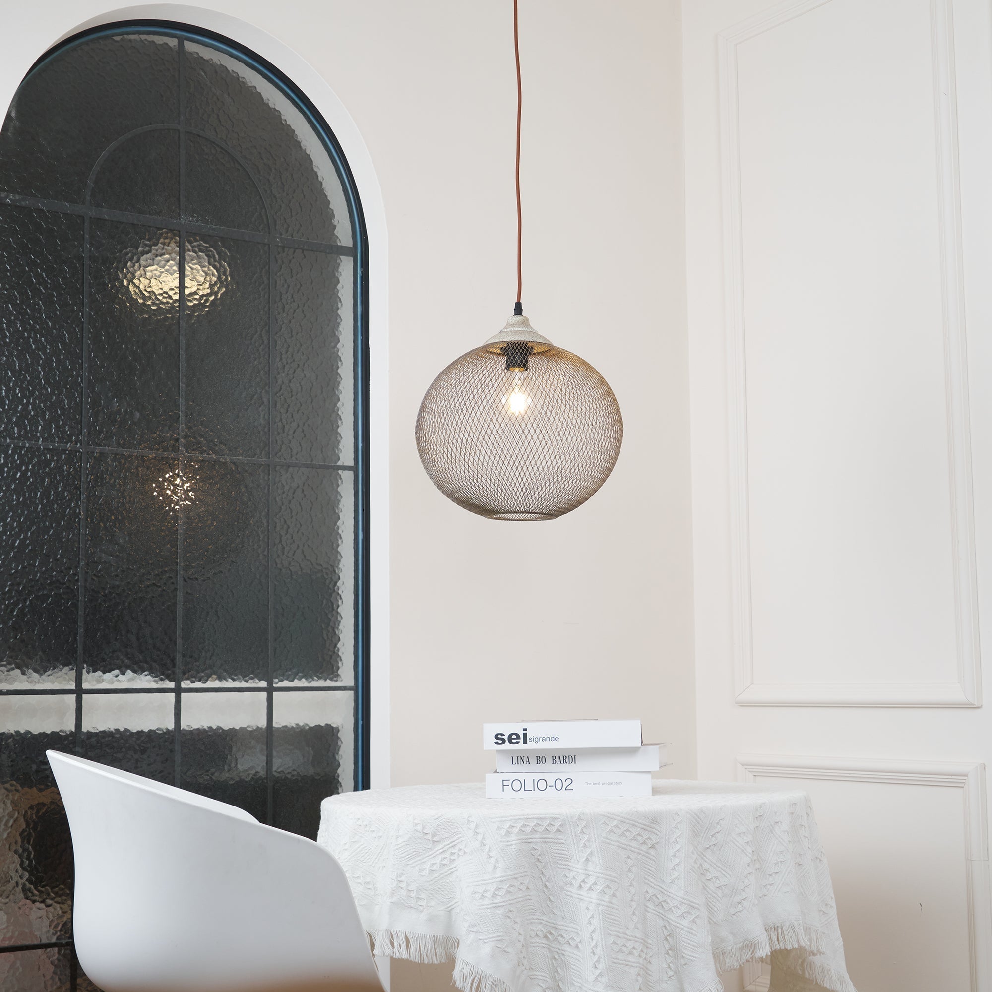 The Clérachic mesh pendant lights a dining nook beside an arched window and a stack of books.