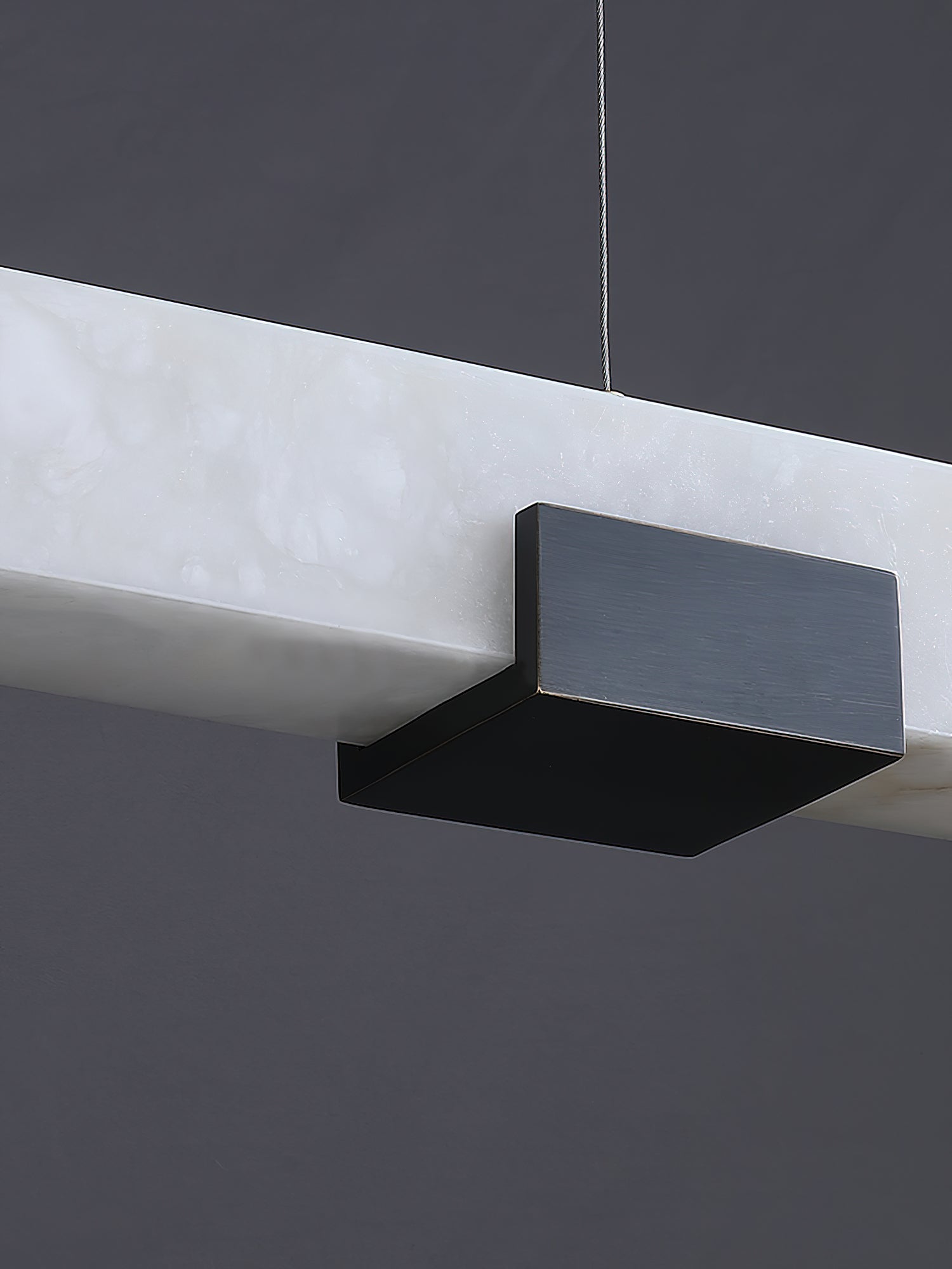 Close view of the Clérachic Avert's matte black brass saddle clamped over the alabaster bar's translucent edge.