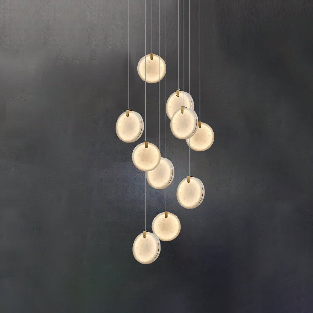 The ten-head Clérachic alabaster pendant lit against a dark wall, each disc glowing evenly across its whole face.