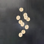 The ten-head Clérachic alabaster pendant lit against a dark wall, each disc glowing evenly across its whole face.