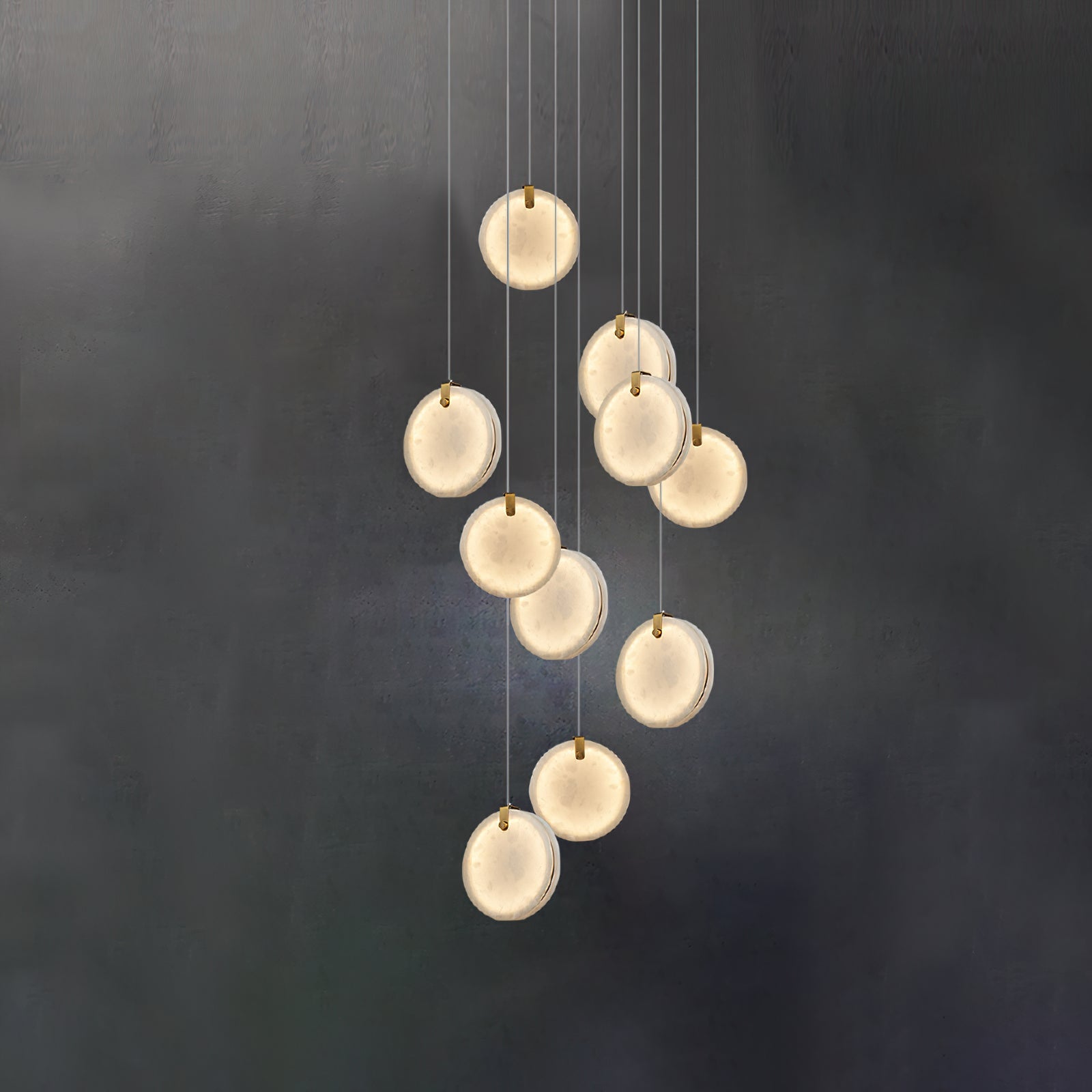 The ten-head Clérachic alabaster pendant lit against a dark wall, each disc glowing evenly across its whole face.