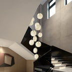 The Clérachic alabaster pendant cluster falling through a stairwell, discs stepping down beside a black glass balustrade.