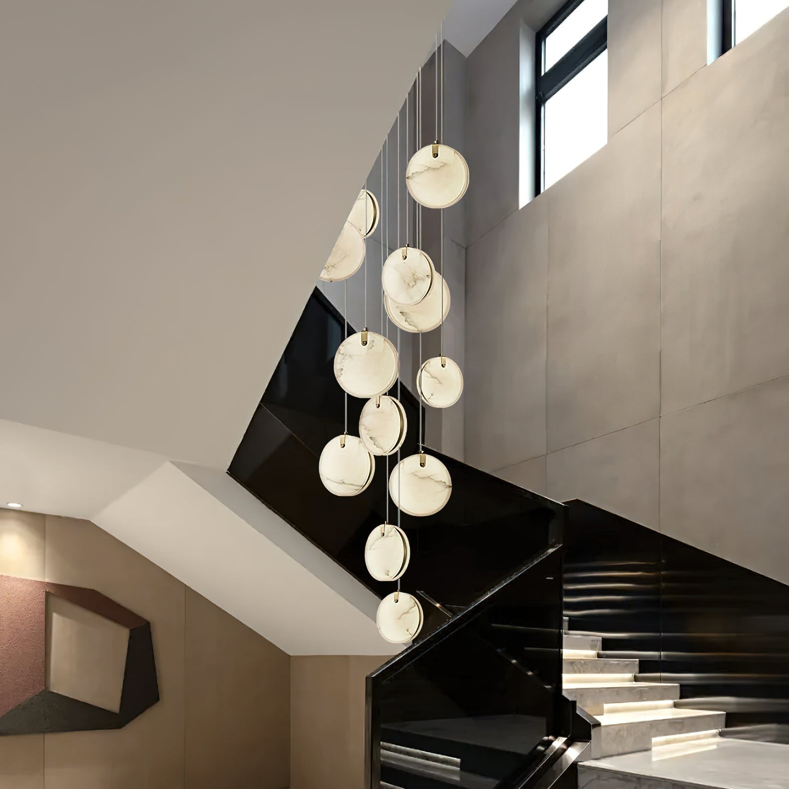 The Clérachic alabaster pendant cluster falling through a stairwell, discs stepping down beside a black glass balustrade.