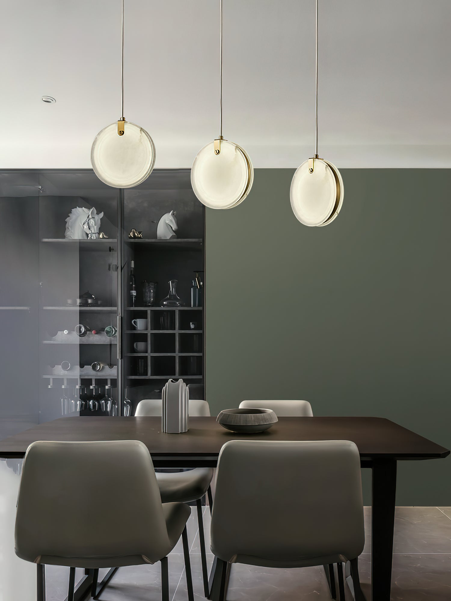 Three Clérachic alabaster pendants over a dark dining table, hung at staggered drops against a deep green wall.