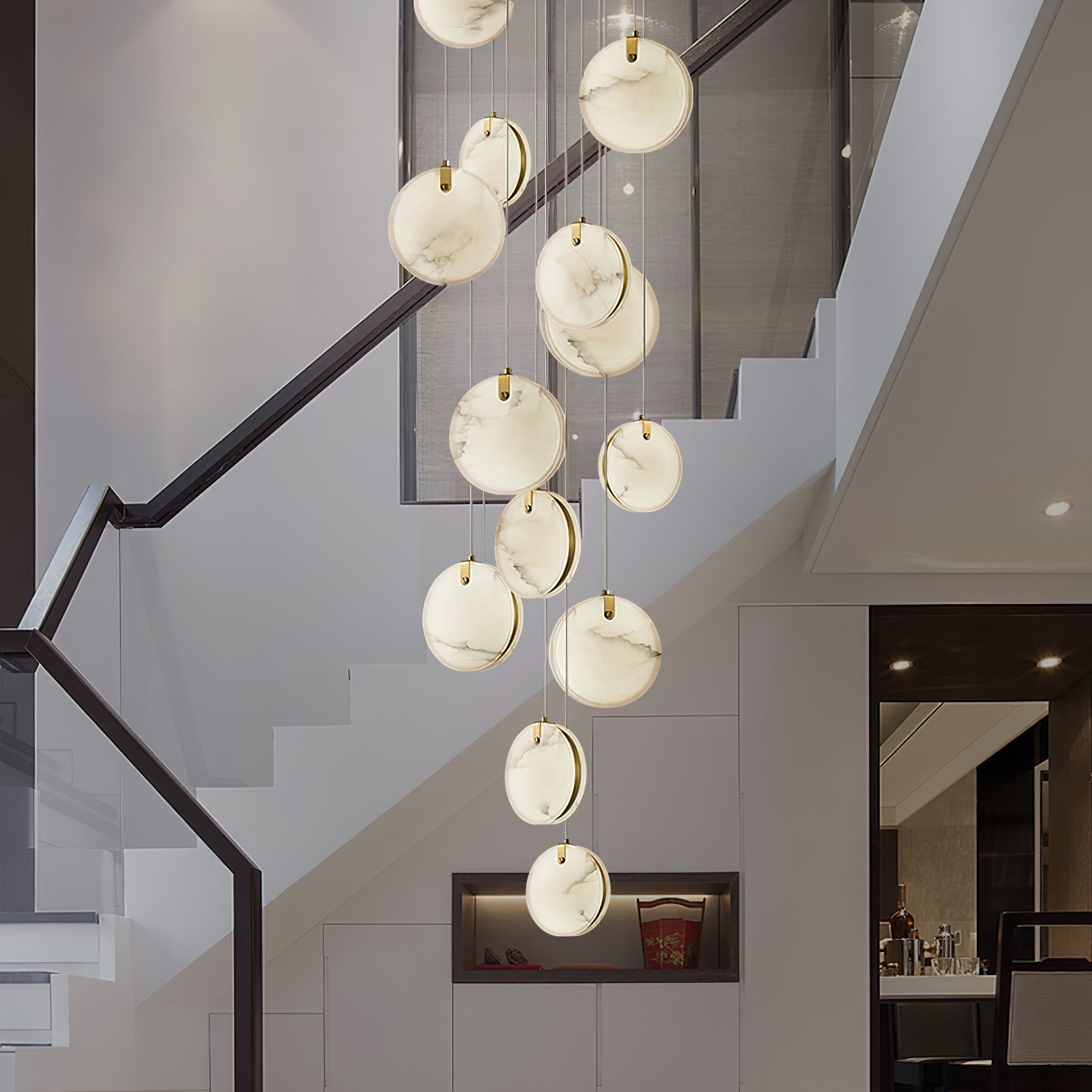 The Clérachic multi-head alabaster pendant spiralling down a white stairwell, twelve discs lit warm from within.