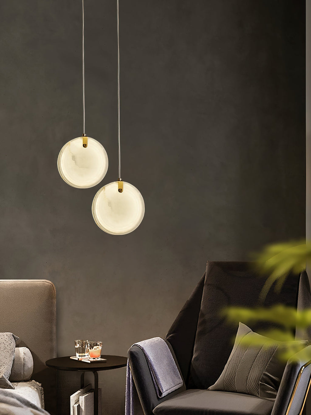 Two Clérachic alabaster pendants hung at different heights above a small drinks table between two armchairs.