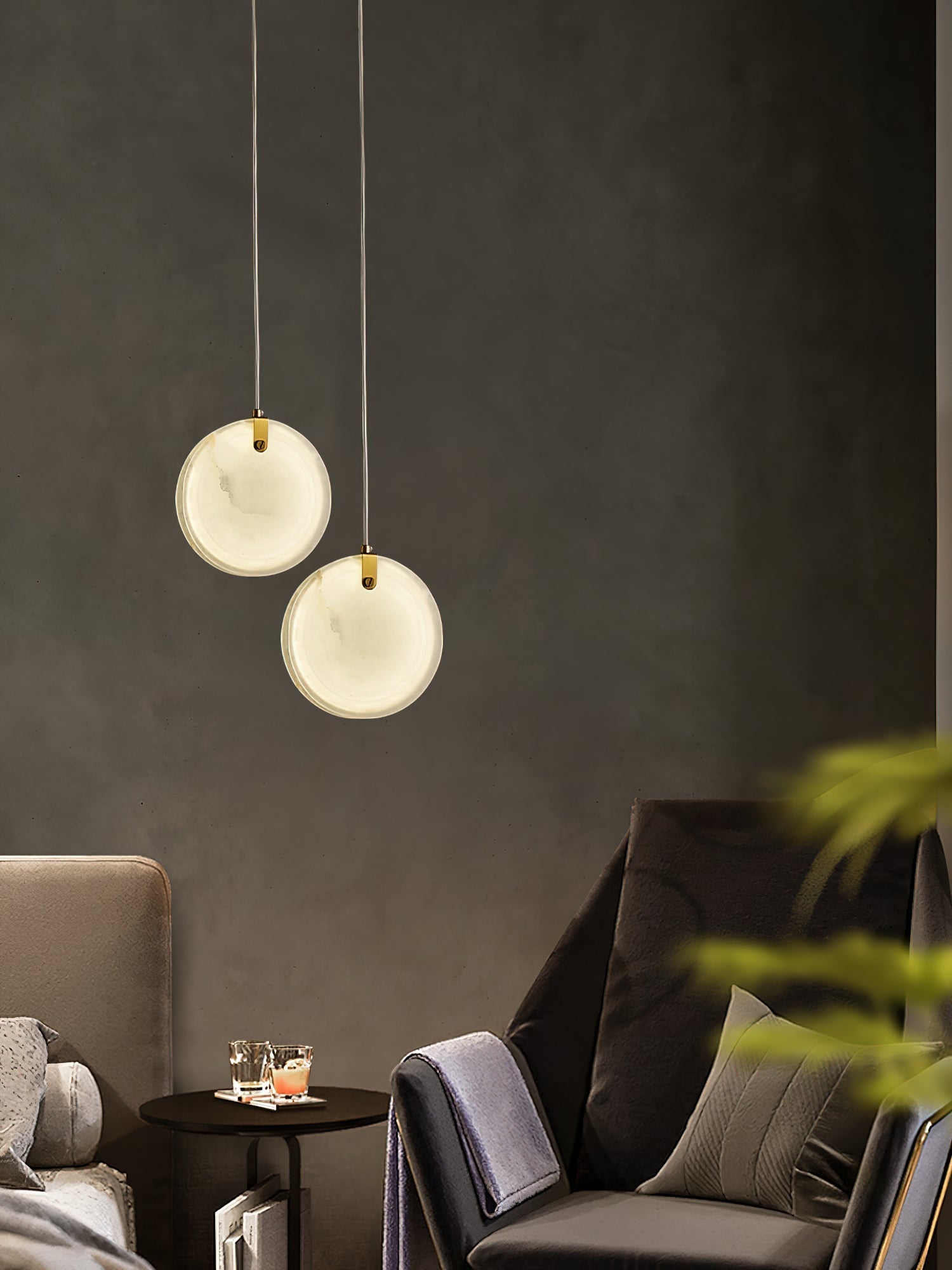Two Clérachic alabaster pendants hung at different heights above a small drinks table between two armchairs.