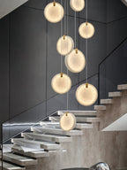 The Clérachic alabaster pendant cluster over floating stone stairs, its discs lit against a charcoal panelled wall.