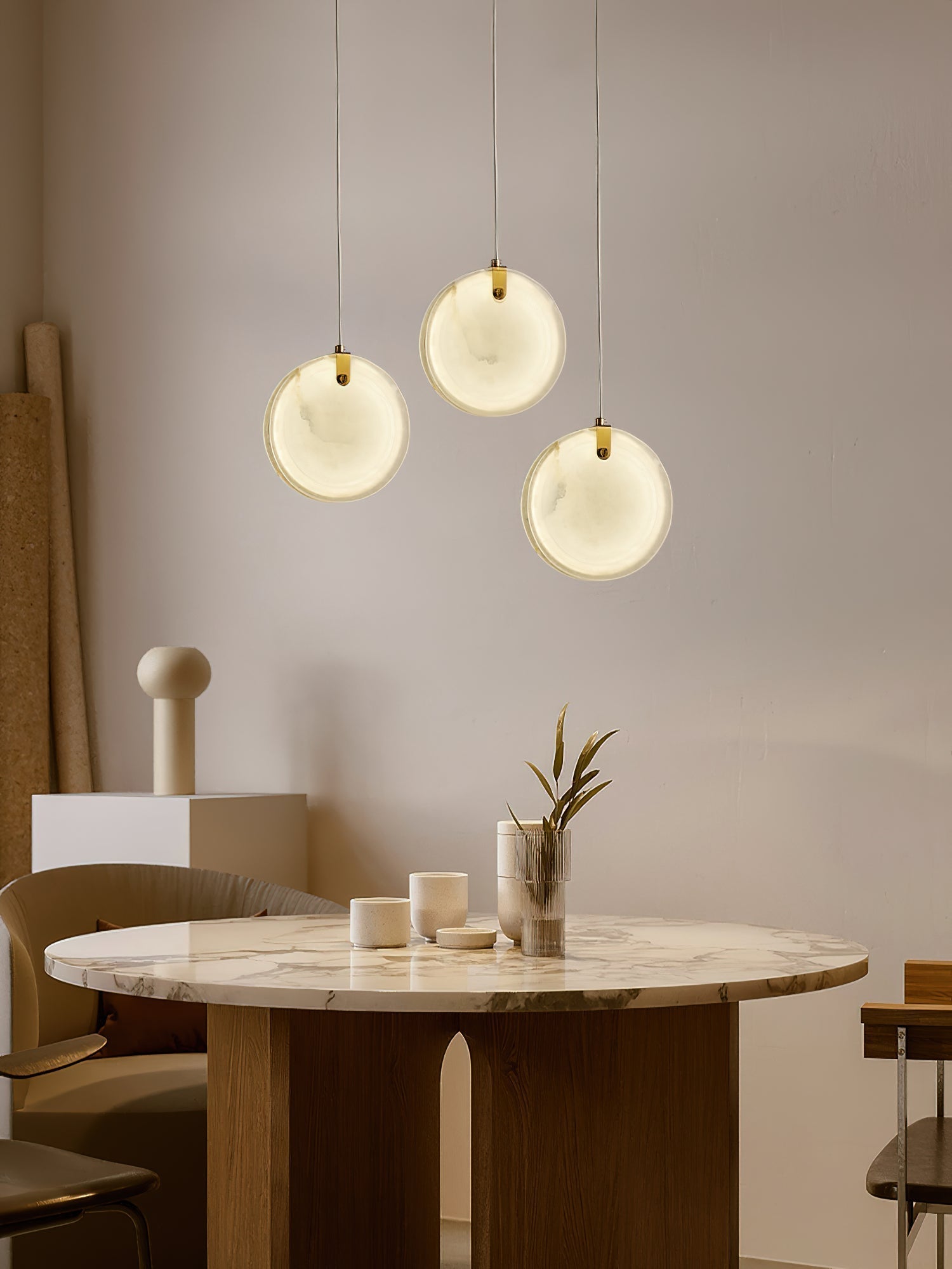 Three Clérachic alabaster pendants above a round marble café table, glowing softly against a bare plaster wall.