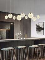 Nine Clérachic alabaster discs of varied size strung in a line above a kitchen island and copper bar stools.
