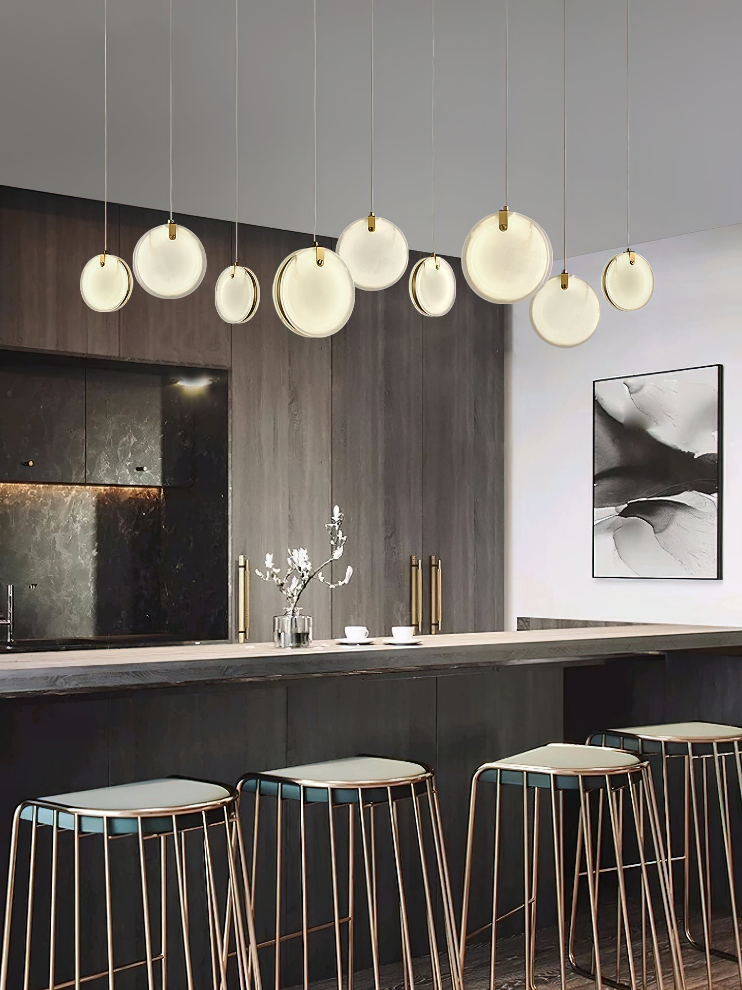 Nine Clérachic alabaster discs of varied size strung in a line above a kitchen island and copper bar stools.