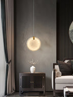 A Clérachic alabaster pendant lit above a dark wood cabinet, its glow spreading across a grey textured wall.