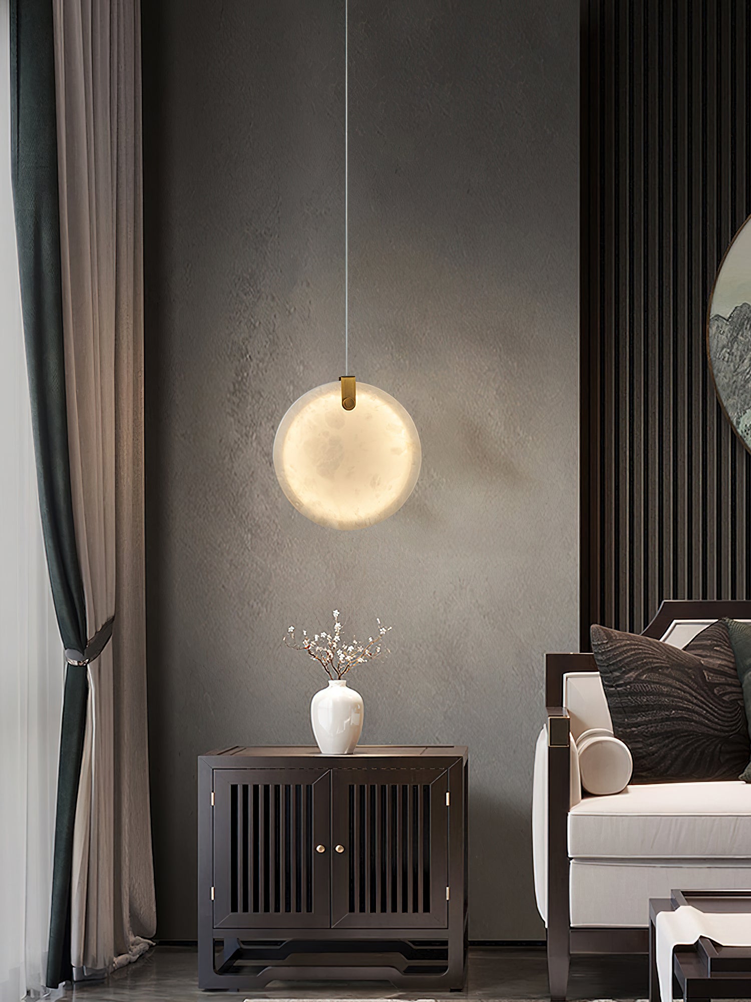 A Clérachic alabaster pendant lit above a dark wood cabinet, its glow spreading across a grey textured wall.