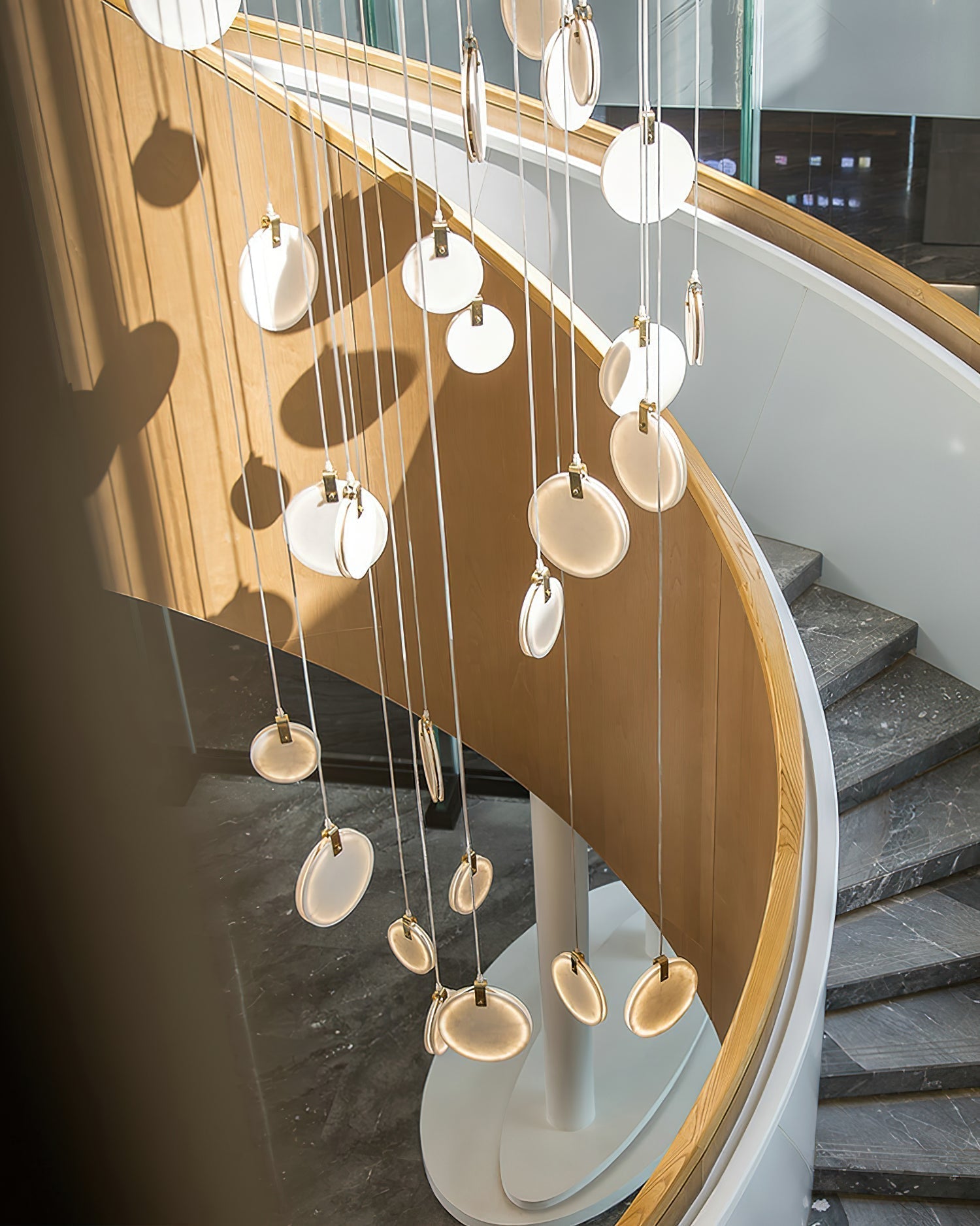 Clérachic alabaster discs seen from above on a curving staircase, casting round shadows across the timber balustrade.