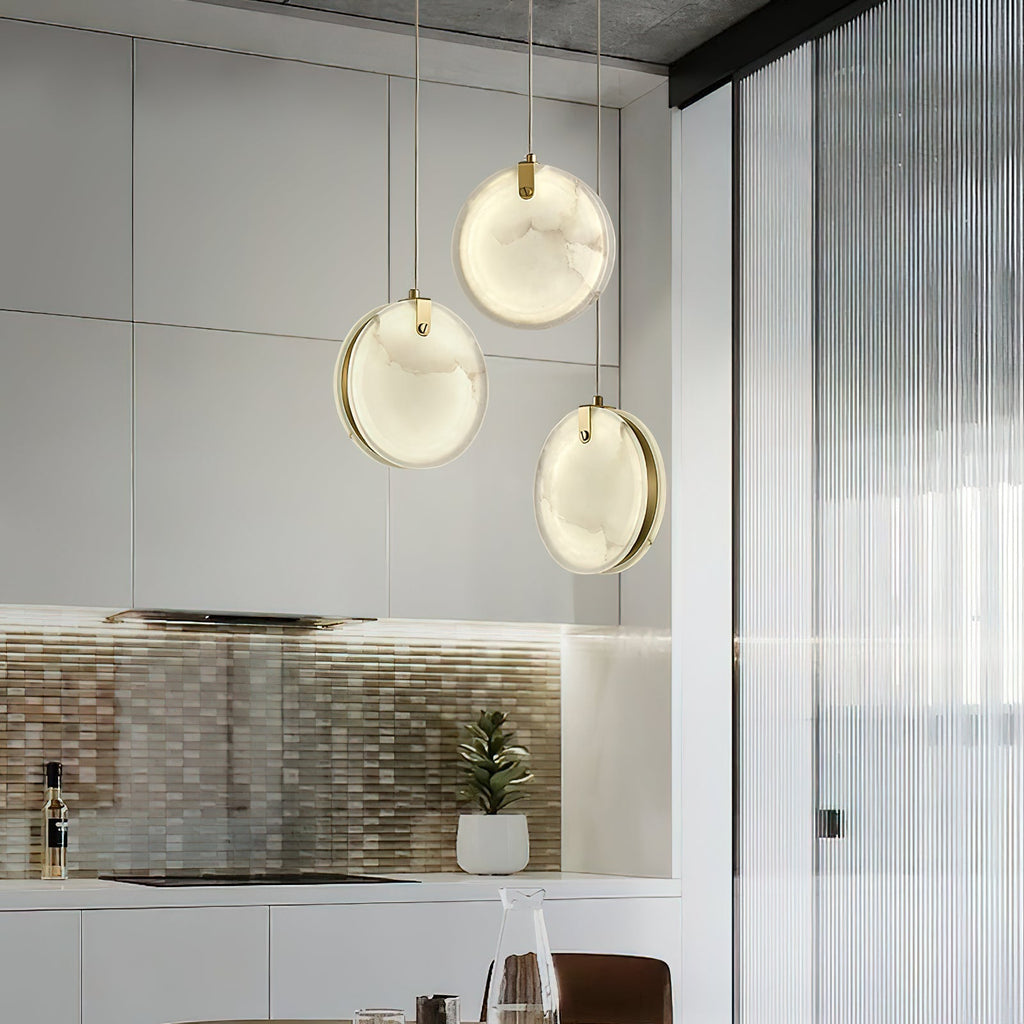 Three Clérachic alabaster pendants clustered in a bright kitchen, brass rims visible behind each glowing disc.