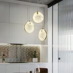 Three Clérachic alabaster pendants clustered in a bright kitchen, brass rims visible behind each glowing disc.