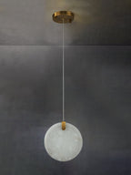 An unlit Clérachic alabaster disc on a long cable from its round brass canopy, chalk-white against bare concrete.