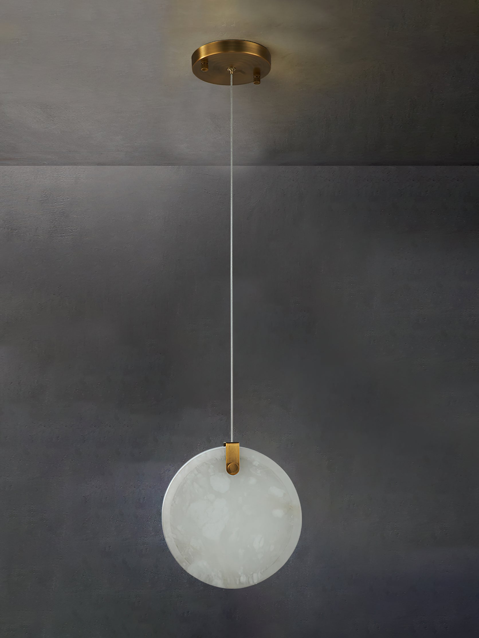An unlit Clérachic alabaster disc on a long cable from its round brass canopy, chalk-white against bare concrete.