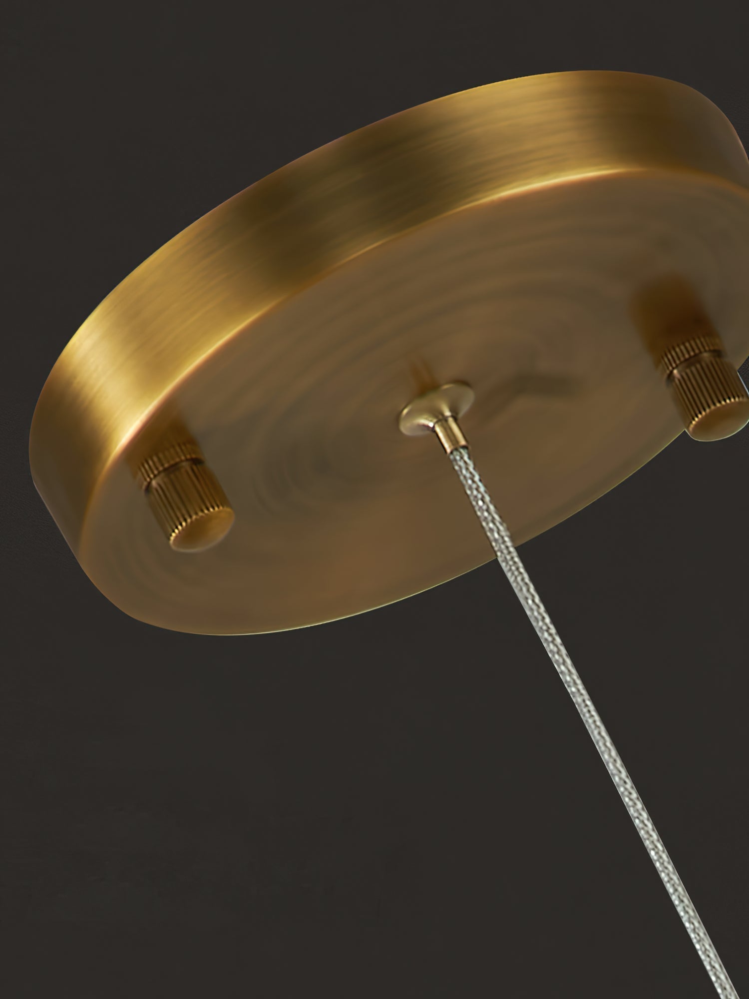 Close-up of the Clérachic pendant's round brass canopy from below, showing the cable thumbscrews that set the drop.