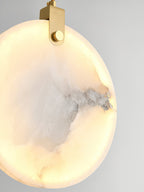 Close-up of a lit Clérachic alabaster disc, grey veining surfacing as dark seams inside the glowing stone.
