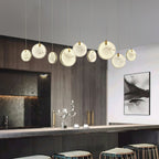 The Clérachic alabaster pendant run of nine discs lit above a long kitchen bar, seen from the room's far side.