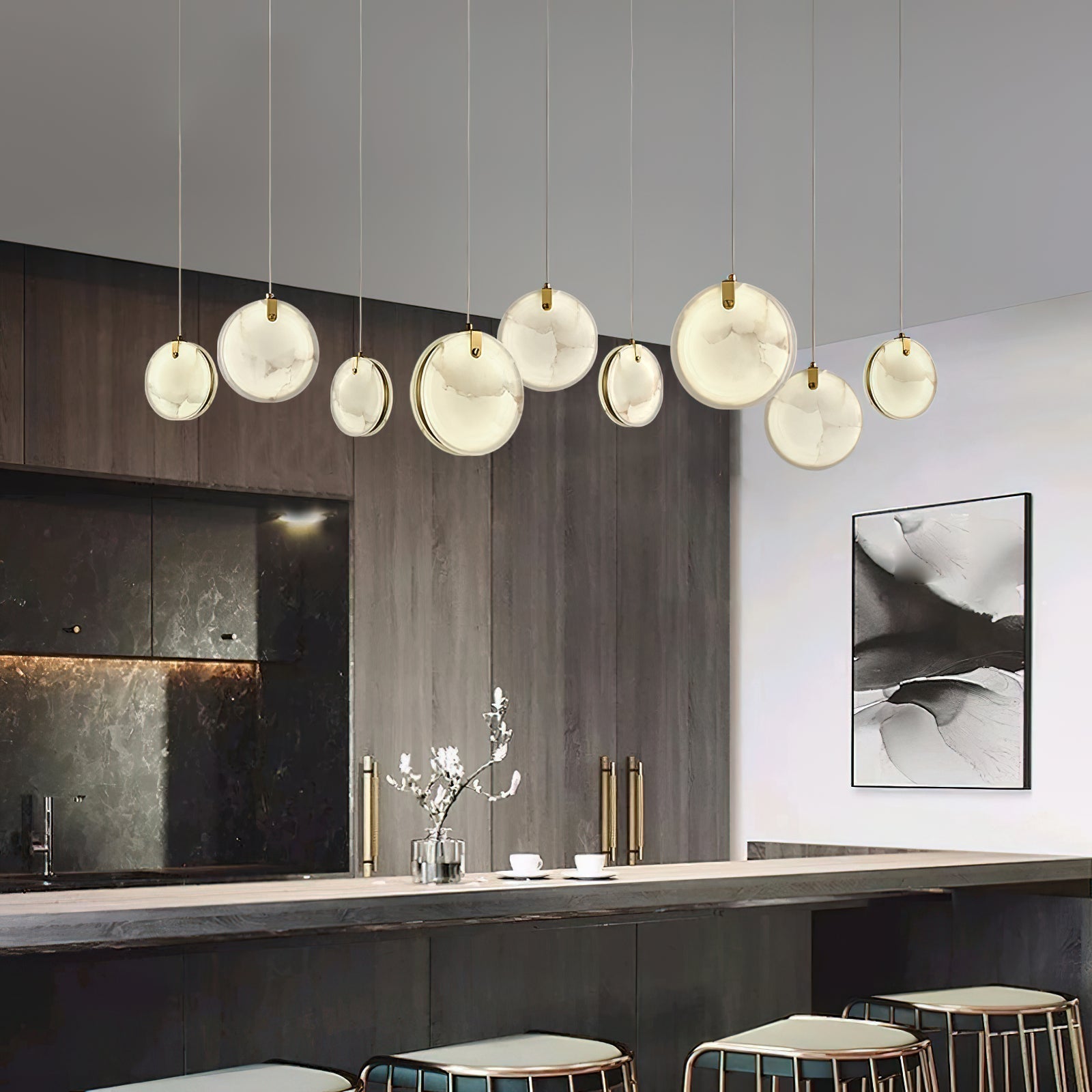 The Clérachic alabaster pendant run of nine discs lit above a long kitchen bar, seen from the room's far side.