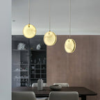 Three Clérachic alabaster pendants above a dark dining table, staggered against a walnut-panelled wall.