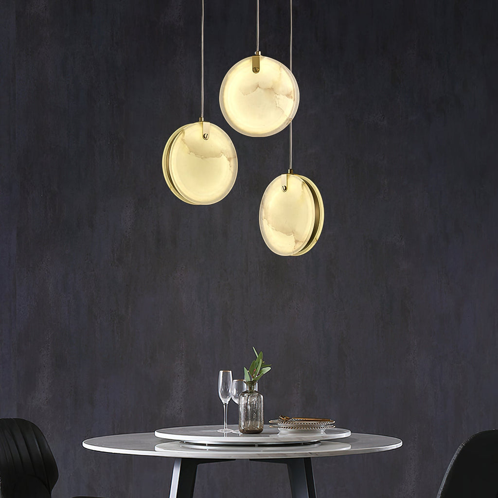 Three Clérachic alabaster discs hung in a loose triangle above a round marble table on a charcoal wall.