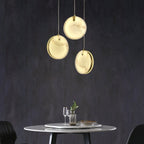 Three Clérachic alabaster discs hung in a loose triangle above a round marble table on a charcoal wall.