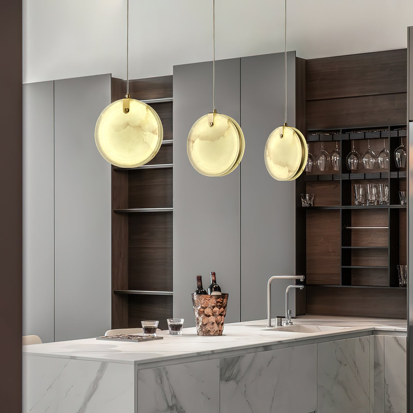 Three Clérachic alabaster pendants lit above a white marble kitchen island in front of a glass-fronted wine store.