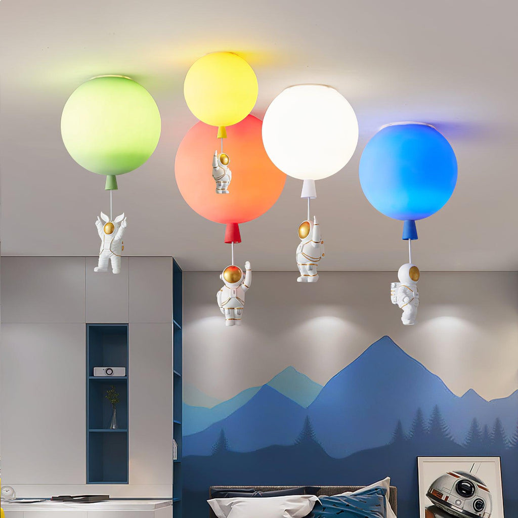 Four Clérachic balloon lights in green, yellow, orange, white and blue float above a bed, each with an astronaut hanging below.
