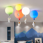 Four Clérachic balloon lights in green, yellow, orange, white and blue float above a bed, each with an astronaut hanging below.