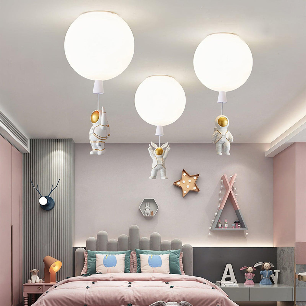 Three white Clérachic balloon ceiling lights with astronaut figures, above a pink bed with a grey padded headboard.