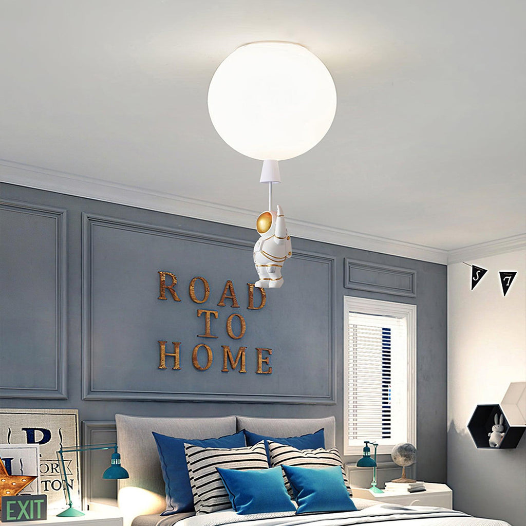 A single white Clérachic balloon light with an astronaut, above a bed with striped cushions and a grey panelled wall.