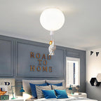 A single white Clérachic balloon light with an astronaut, above a bed with striped cushions and a grey panelled wall.